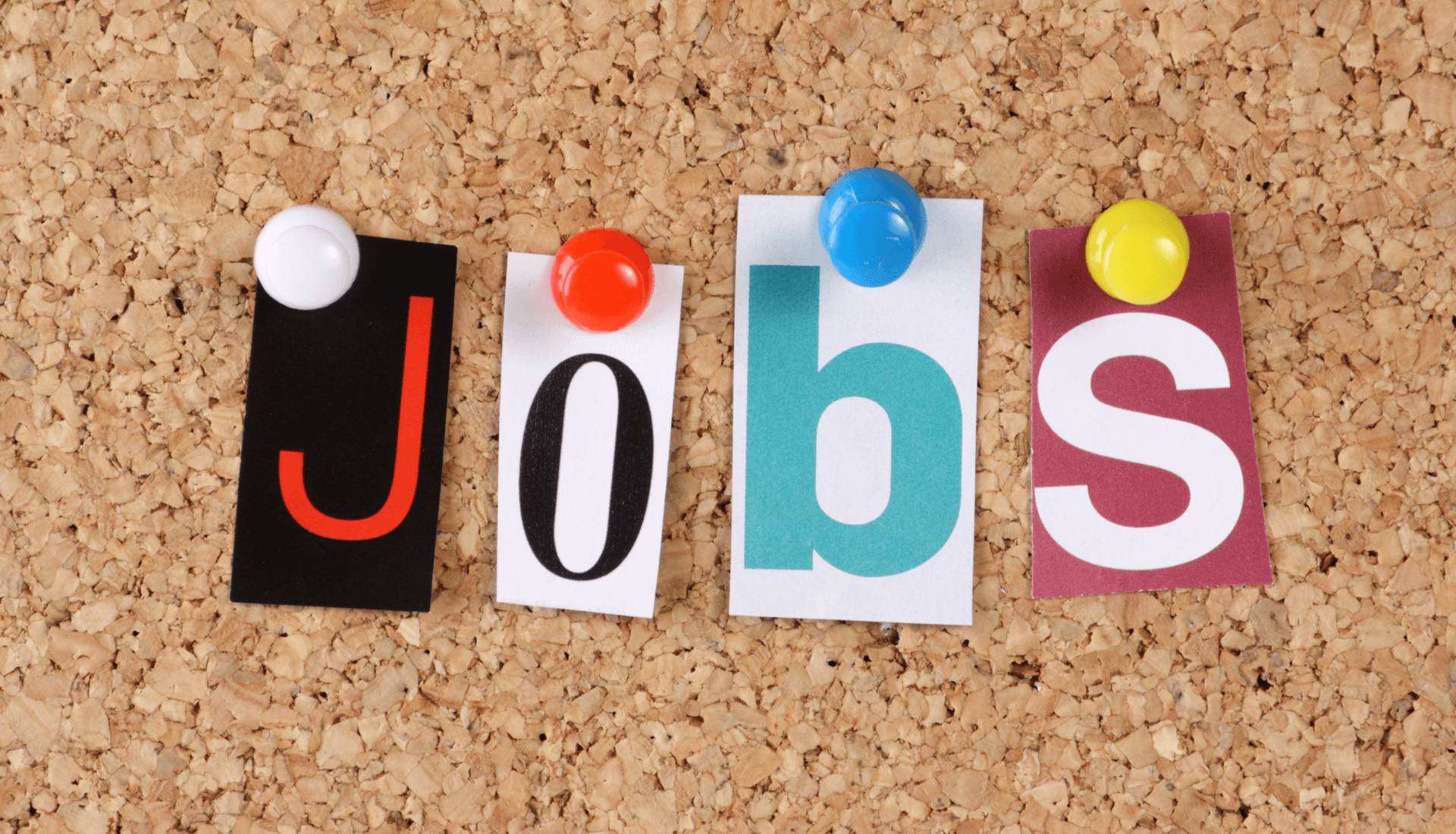 letters cut out from a magazine reading the word 'jobs' and pinned on a corkboard.