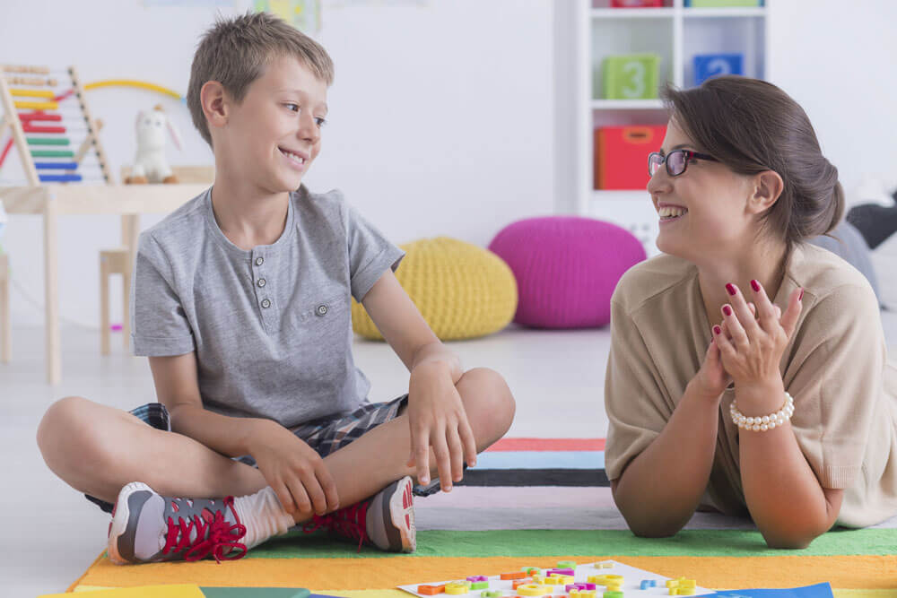 Child and adult sitting and laying on the floor talking while playing with letters on the mat.